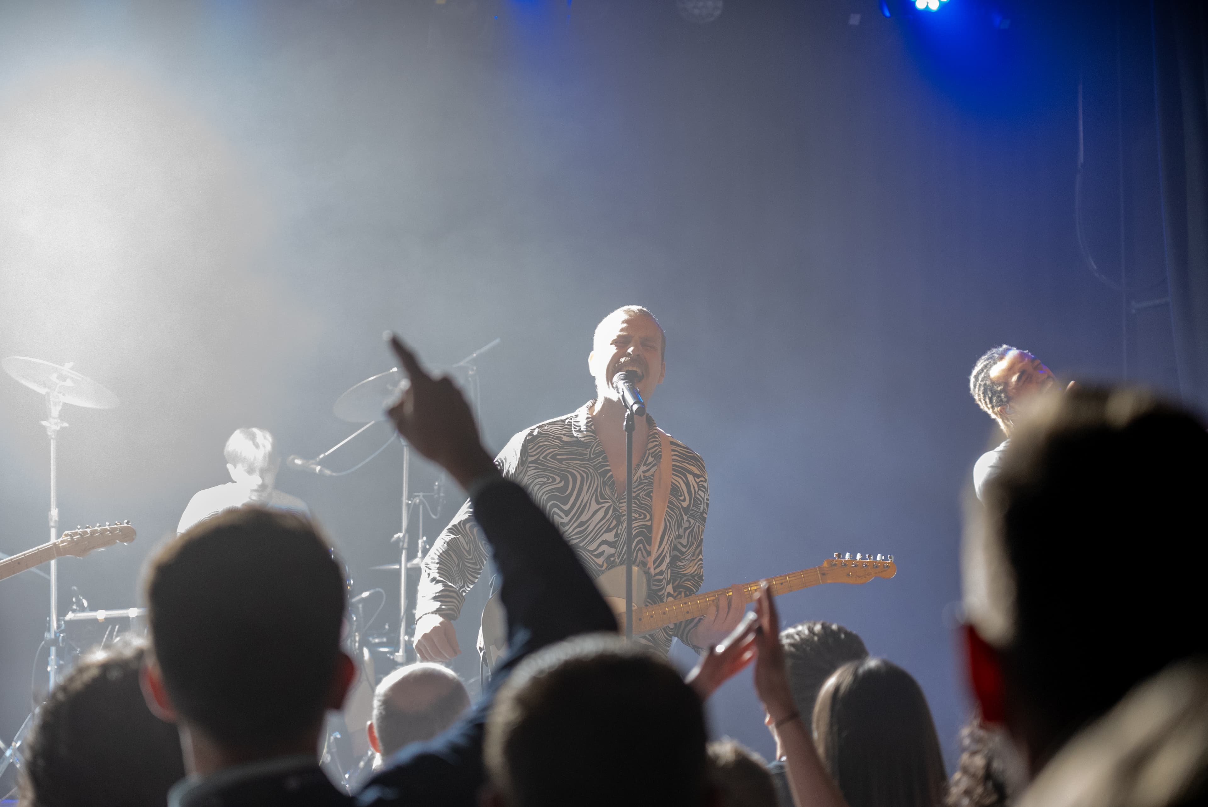 A singer playing electric guitar as audience members raise their hands at a HelloStavanger concert.